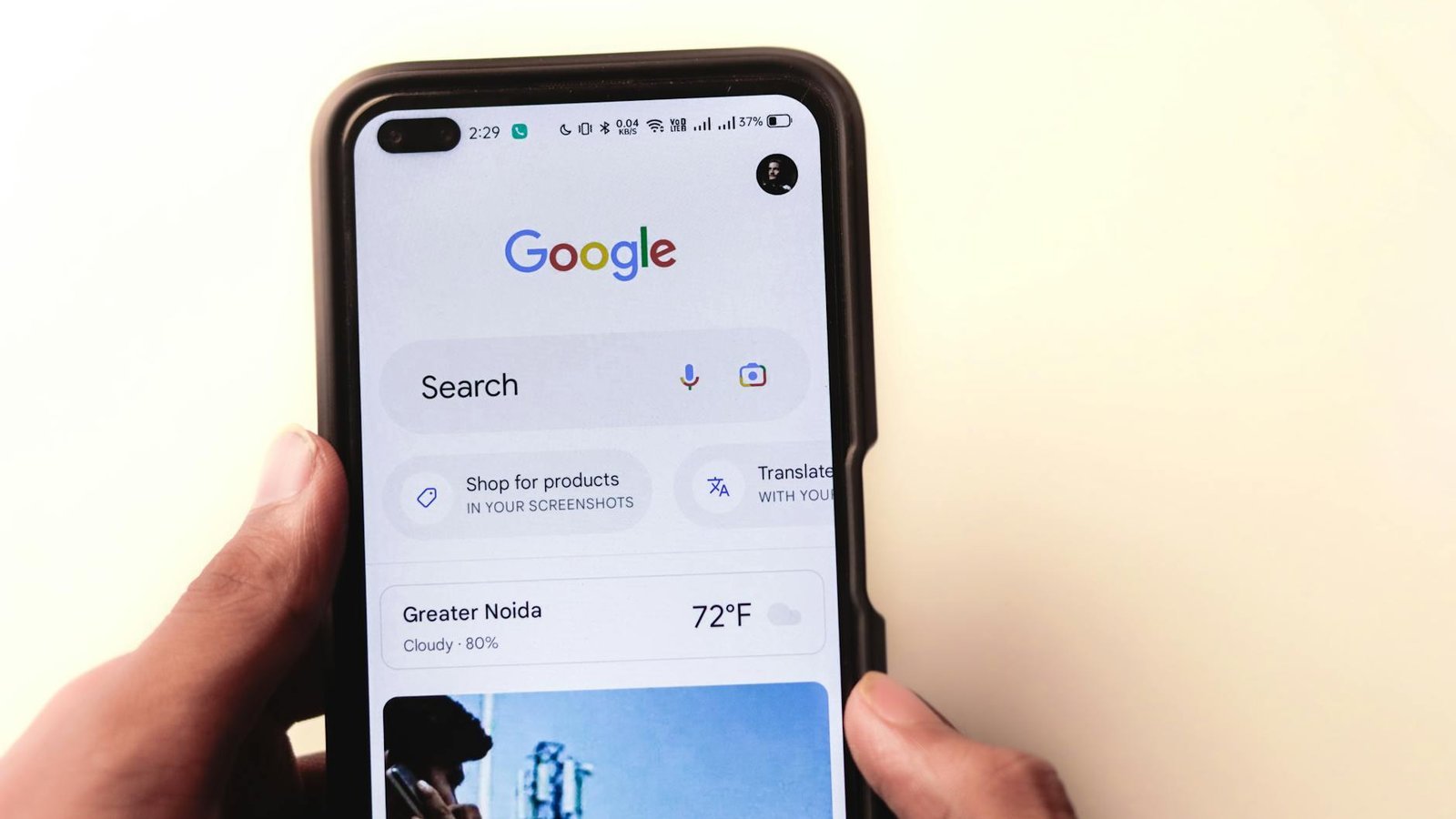 A close-up of a hand holding a smartphone with Google search displayed on the screen.