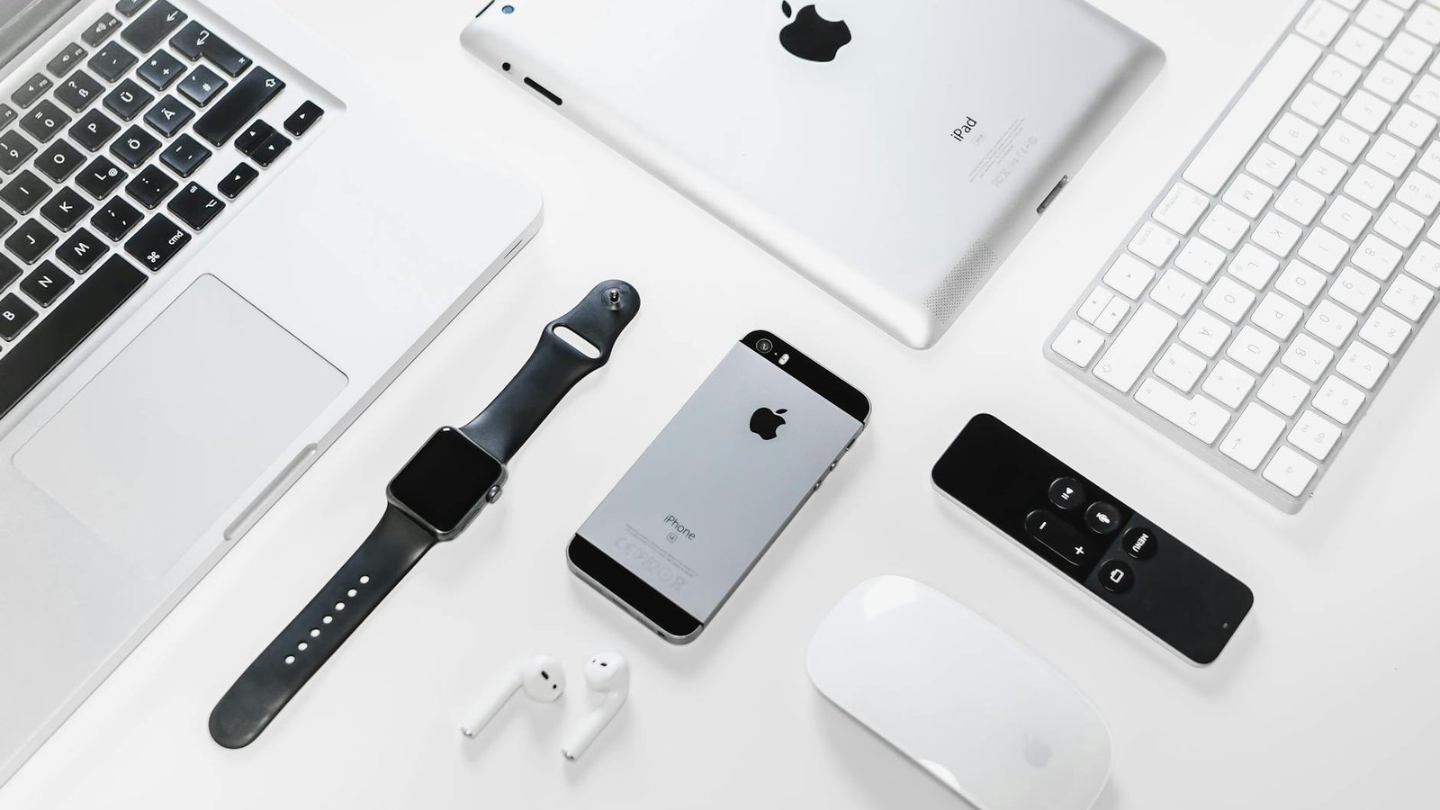 Flat lay of Apple devices including iPhone, iPad, MacBook, and Watch on a white surface, ideal for tech enthusiasts.
