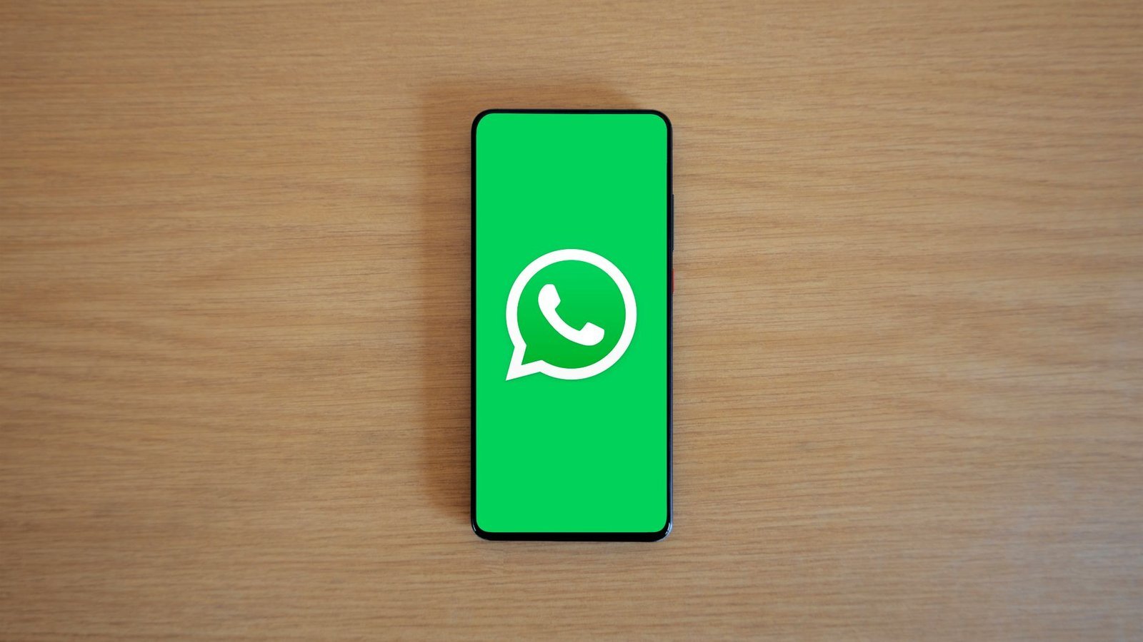 WhatsApp logo sur écran de smartphone posé sur bureau en bois