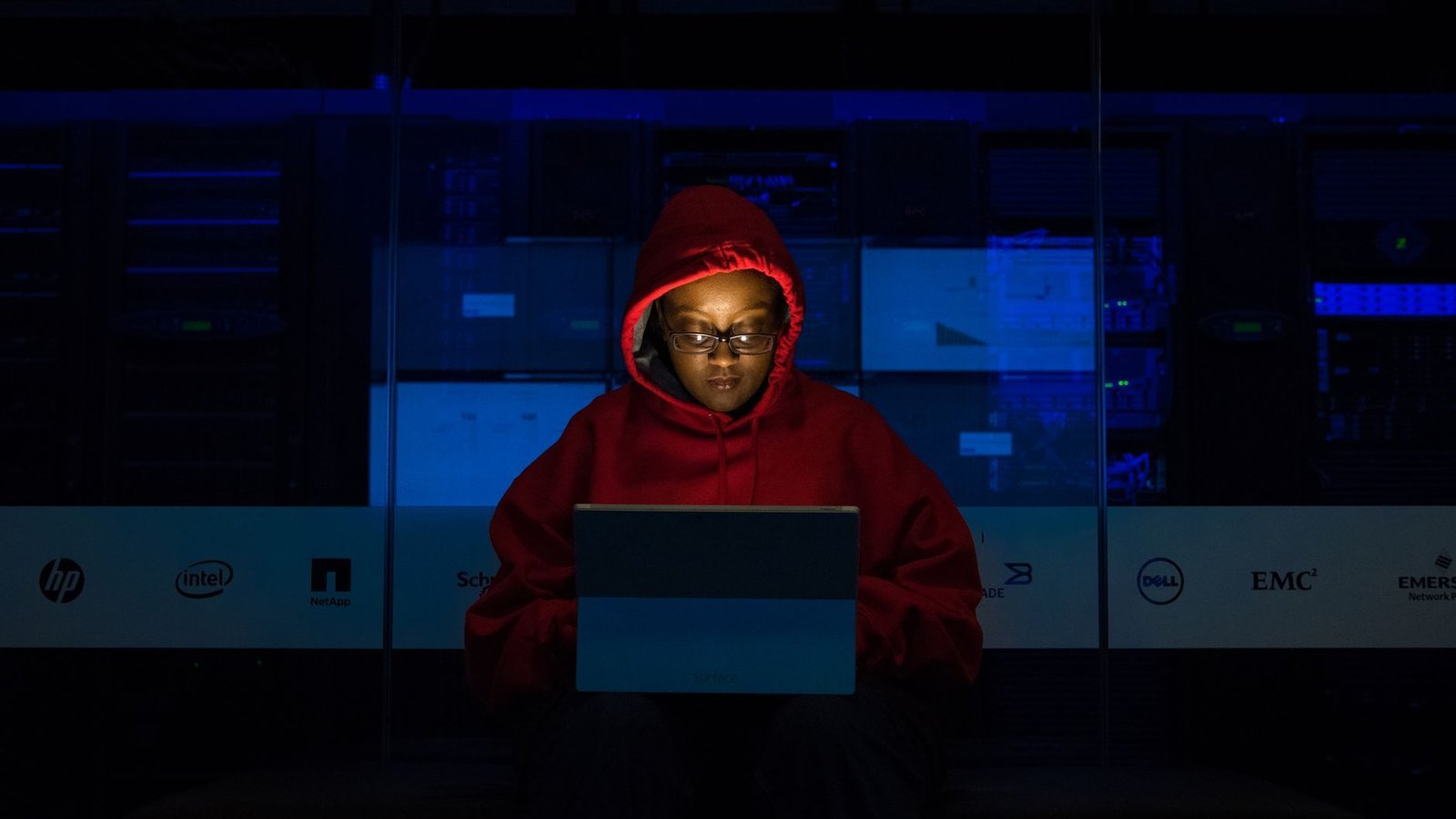 Hacker faille critique — personne en capuche devant laptop dans salle serveurs