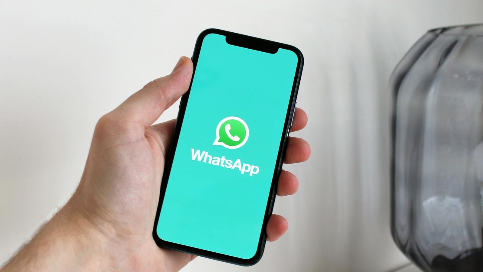 WhatsApp messages éphémères sur iPhone tenu en main avec logo et fond turquoise
