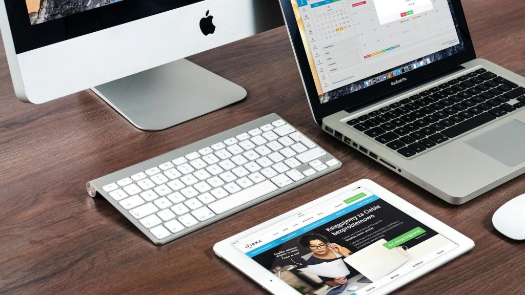 A sleek office desk setup featuring Apple devices: iMac, MacBook, and iPad.