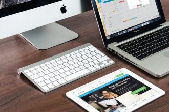 A sleek office desk setup featuring Apple devices: iMac, MacBook, and iPad.