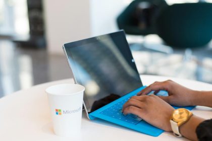 Hands typing on a blue keyboard with a branded cup on a table.