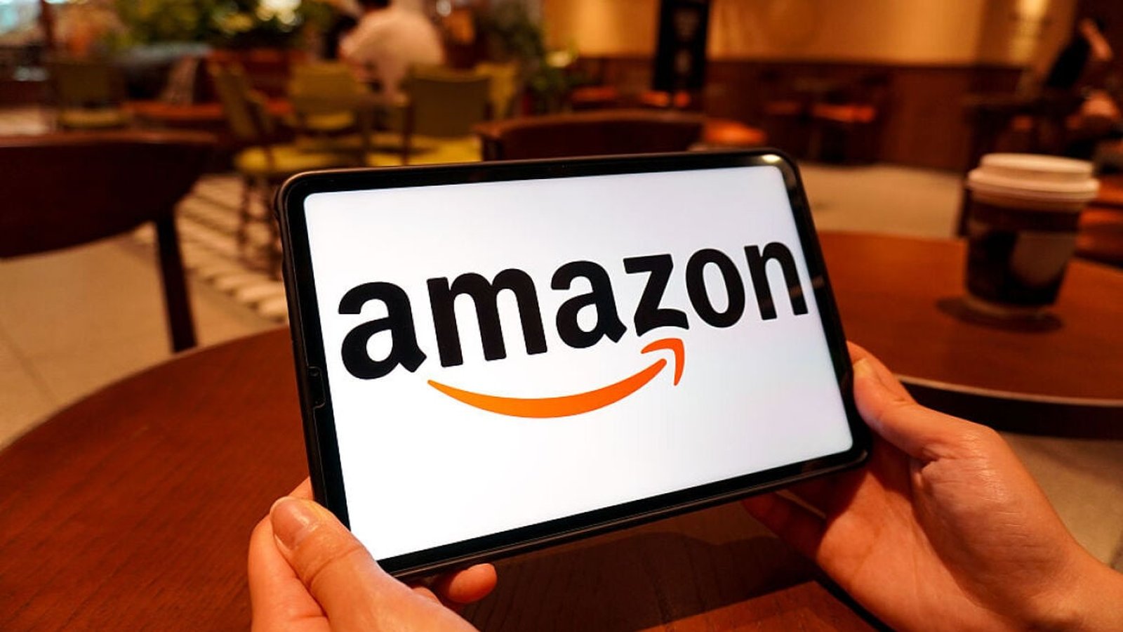 Logo Amazon sur smartphone tenu en mains dans un café